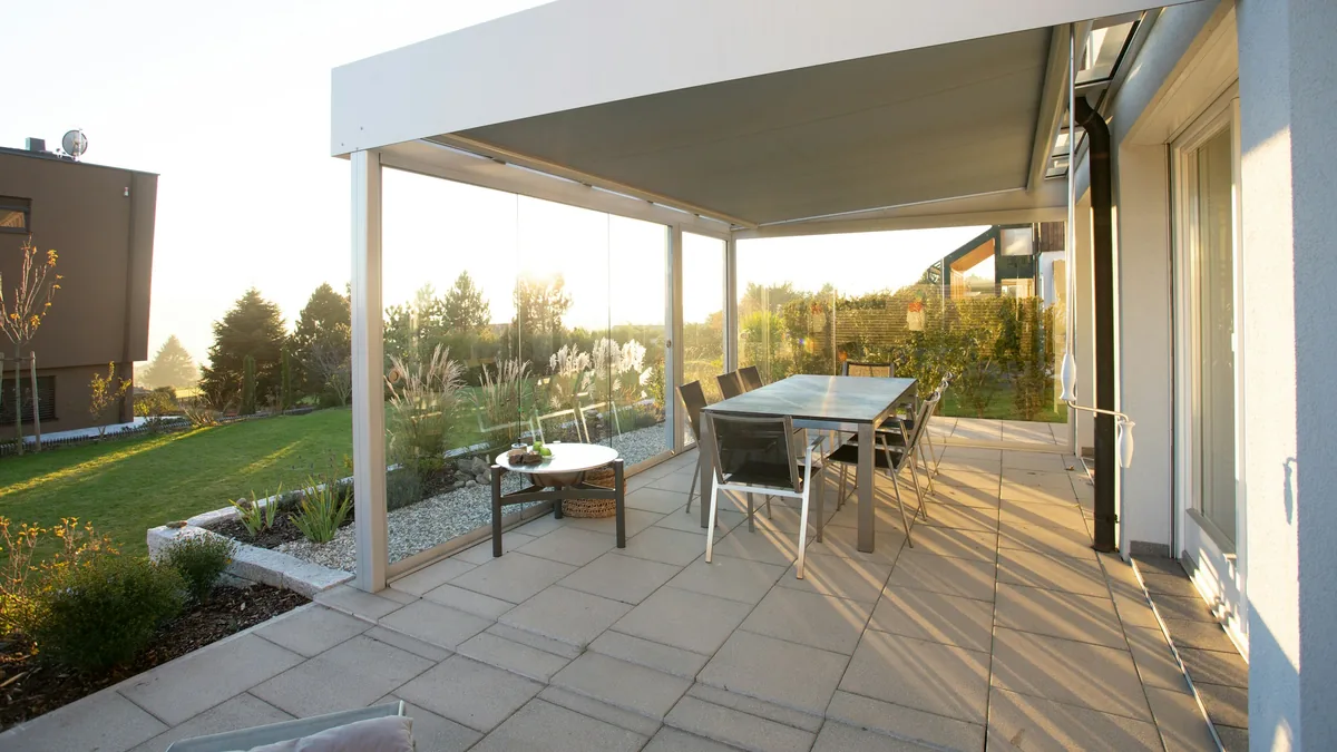 Terrasoverkapping aan een woning met glazen schuifwanden, een tuintafel met stoelen en uitzicht op het gazon